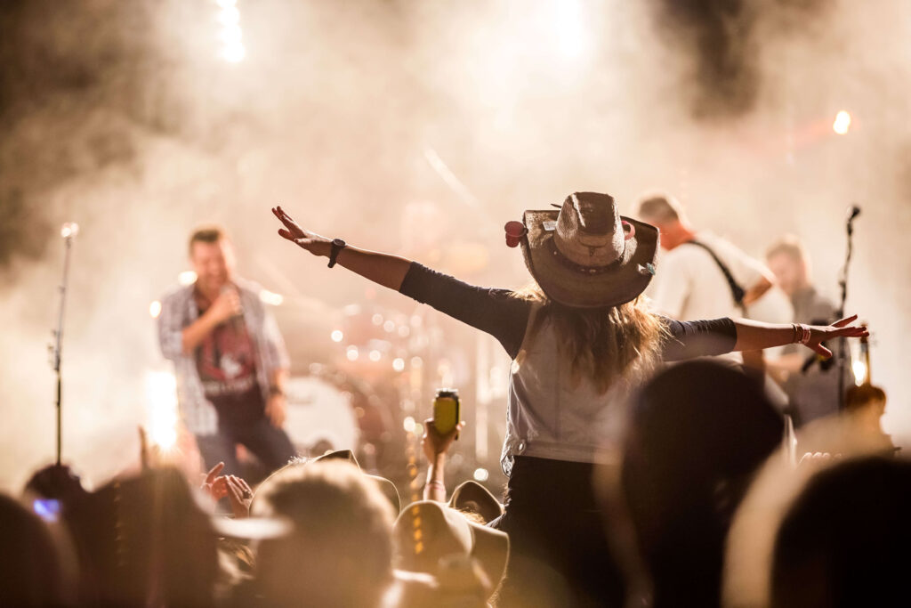 Girl wearing a cowboy hat with her arms outstretched at a country music concert 